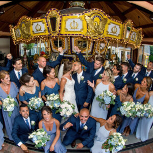 A bridal party inside of a carousel looking at a bride and groom kissing